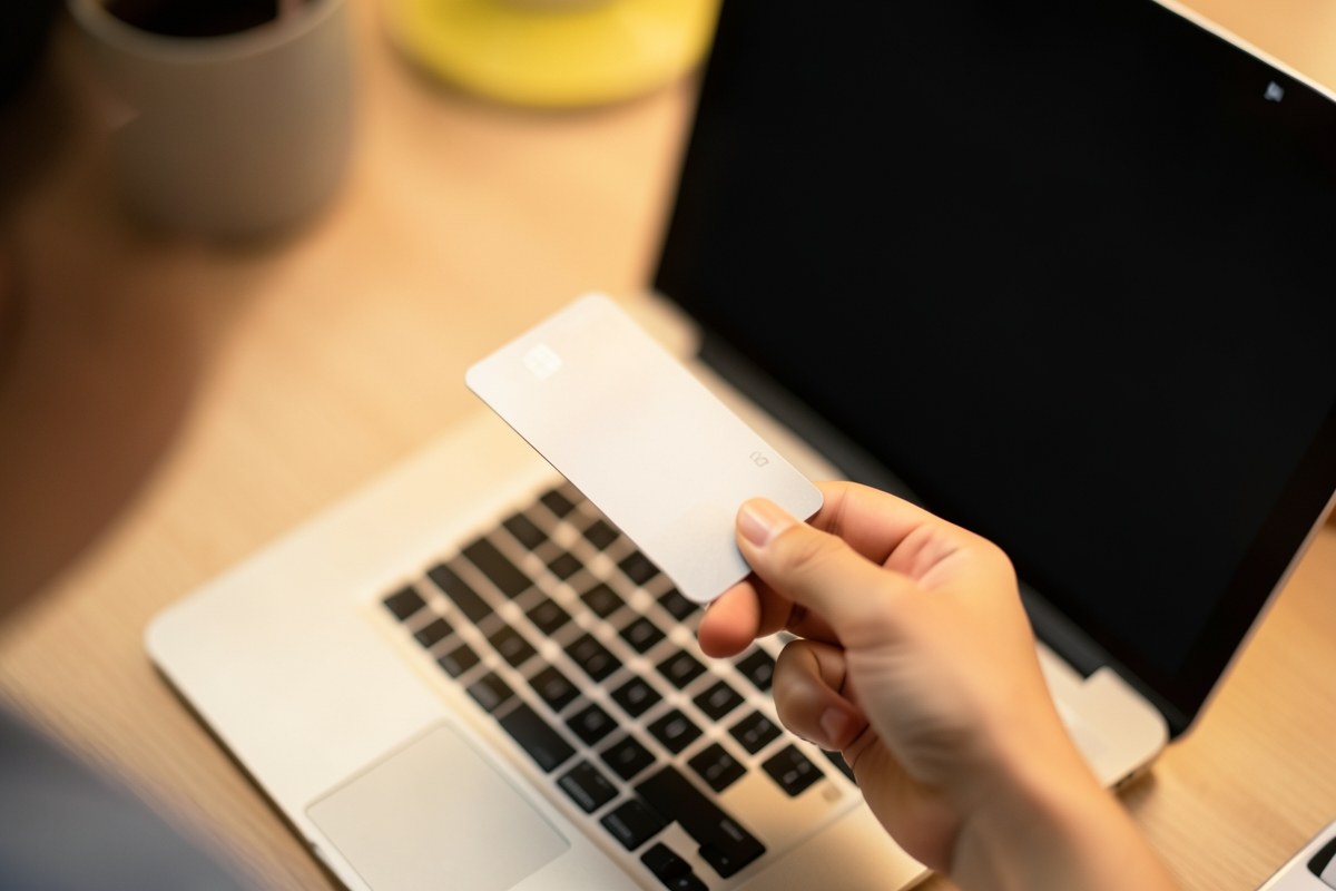 A laptop mid-transaction with a hand holding a credit card, but the screen is blank and no personal info is visible.